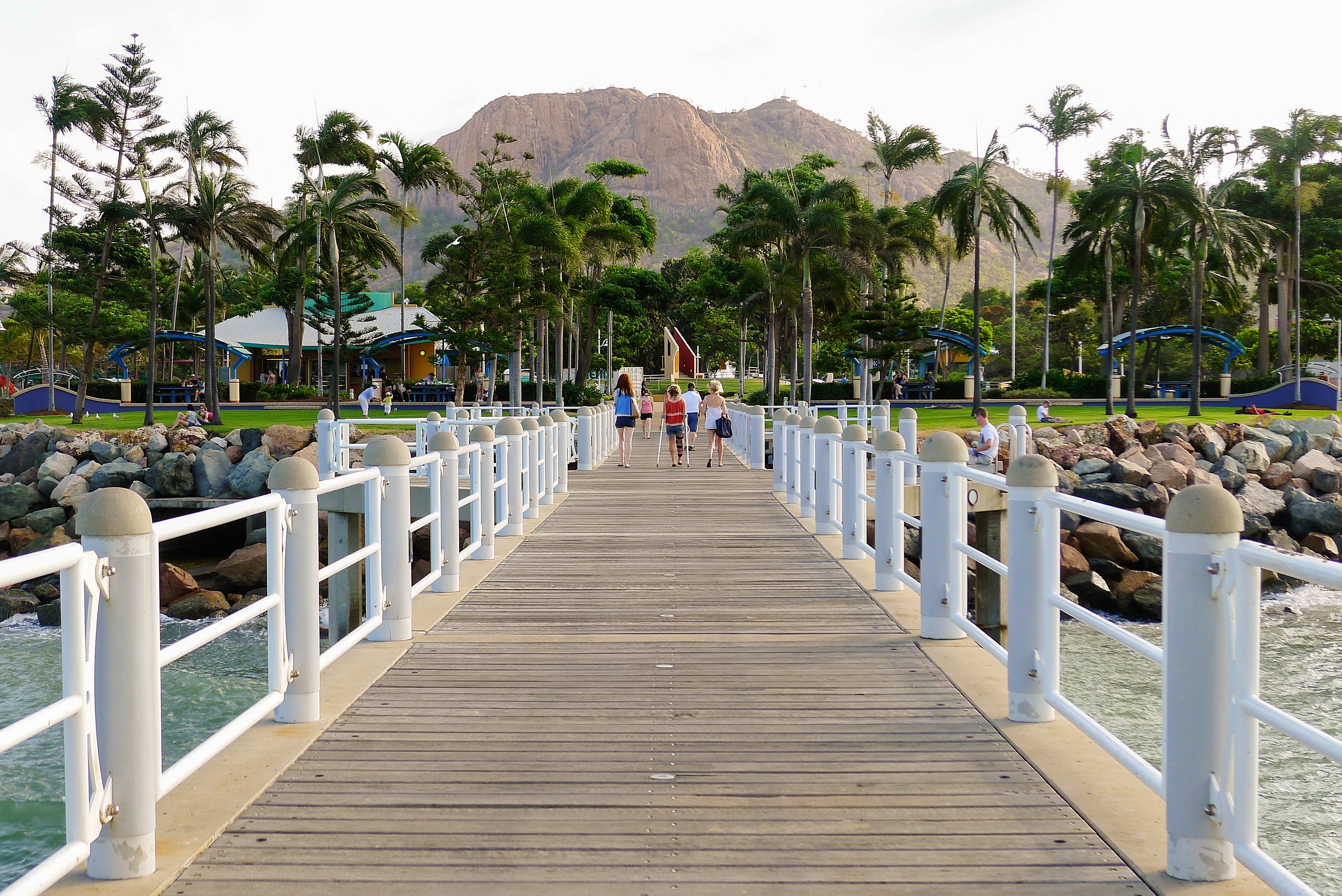 Wooden pier with white railings leading to the Strand, Townsville with Castle hill in the background.